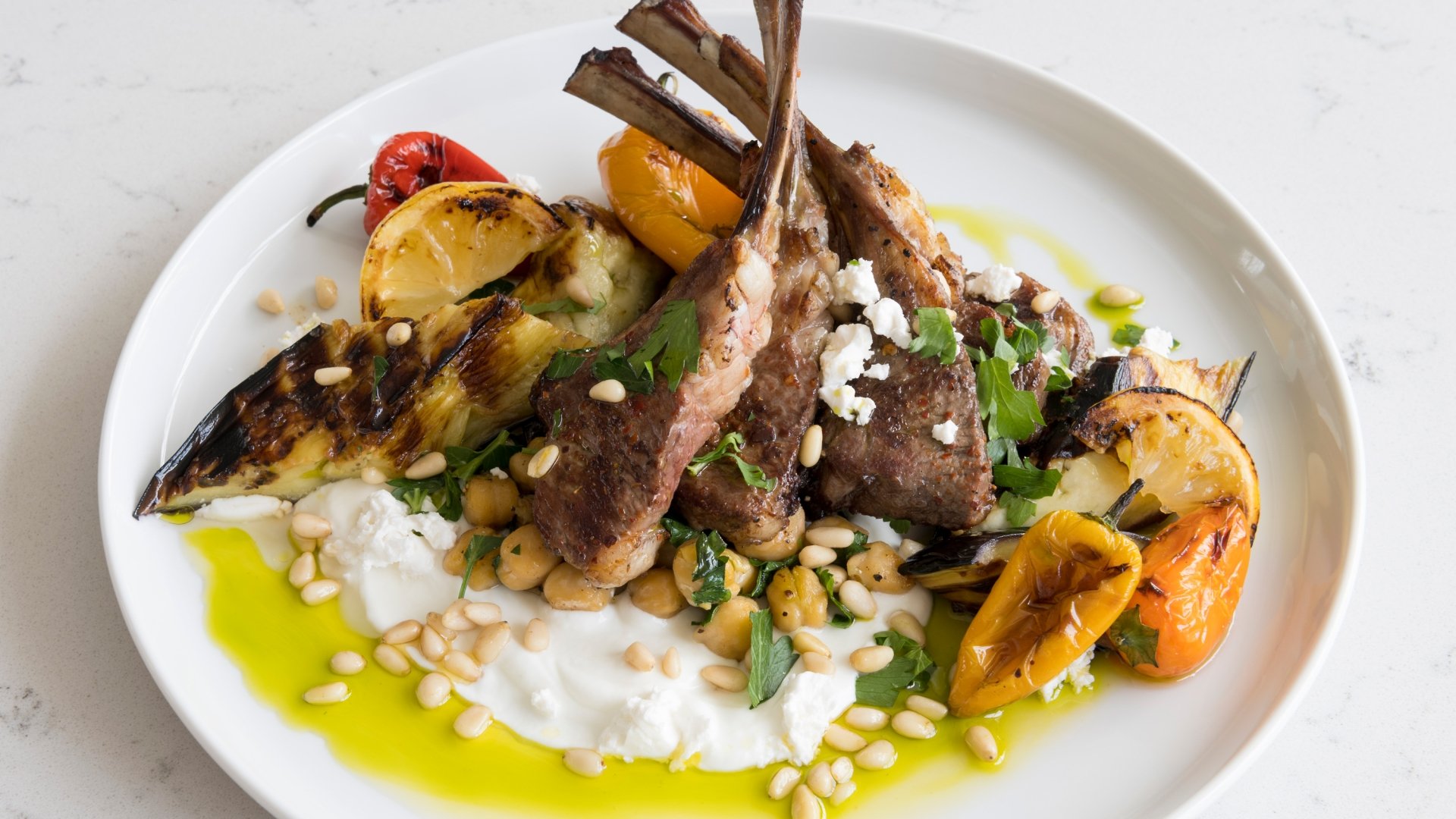 A mediterranean plate featuring a variety of meat, vegetables, and yogurt.